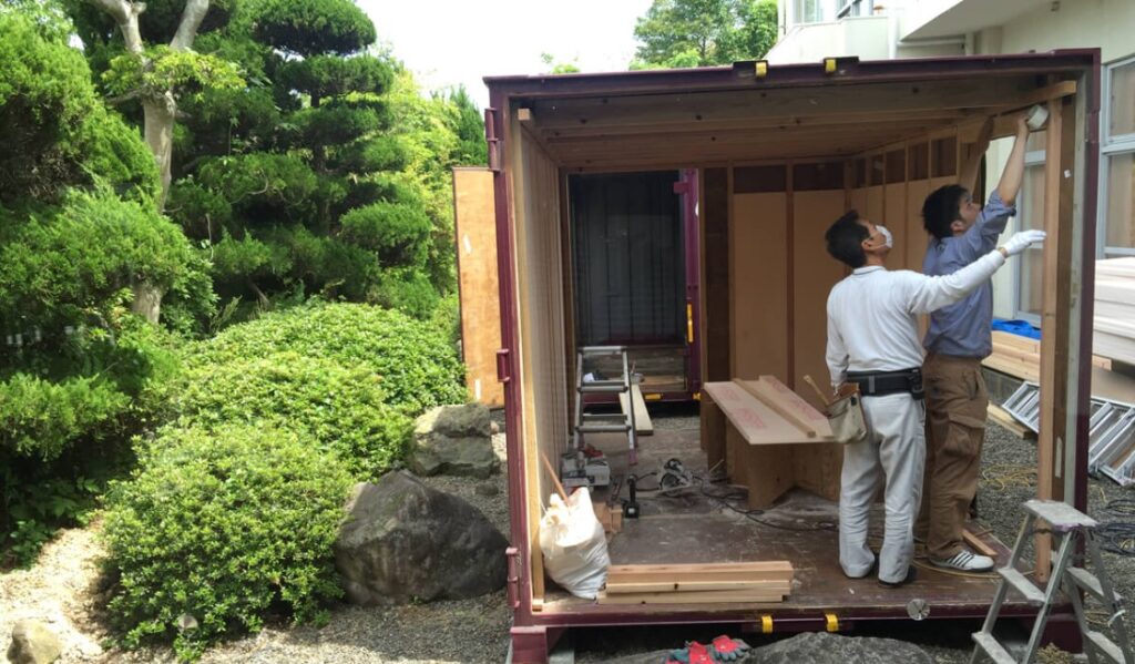 てしま旅館の中庭にある猫の家と猫の世話をする手島姫萌さん