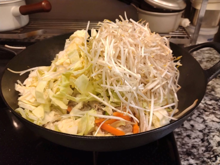 大きめの中華鍋で家族用の焼きそばと小麦不使用のソバめし用の大量の具材を炒めている様子